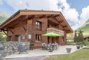 Un chalet in legno con balcone, sedute all'aperto e un muro in pietra.
