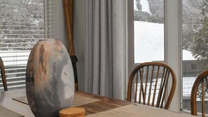 Un coin repas avec une grande table, des chaises en bois, un vase et une vue sur un paysage enneigé par de grandes fenêtres.