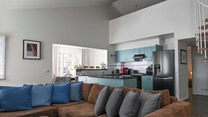Un salon moderne avec un grand canapé d’angle marron, une cuisine aux armoires de couleur turquoise et un escalier menant à un autre niveau.