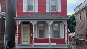 A red two-story house with white trim, a front porch, and a yellow door. - Poe Themed Home Close to Beaches and DE Turf (Milford)
