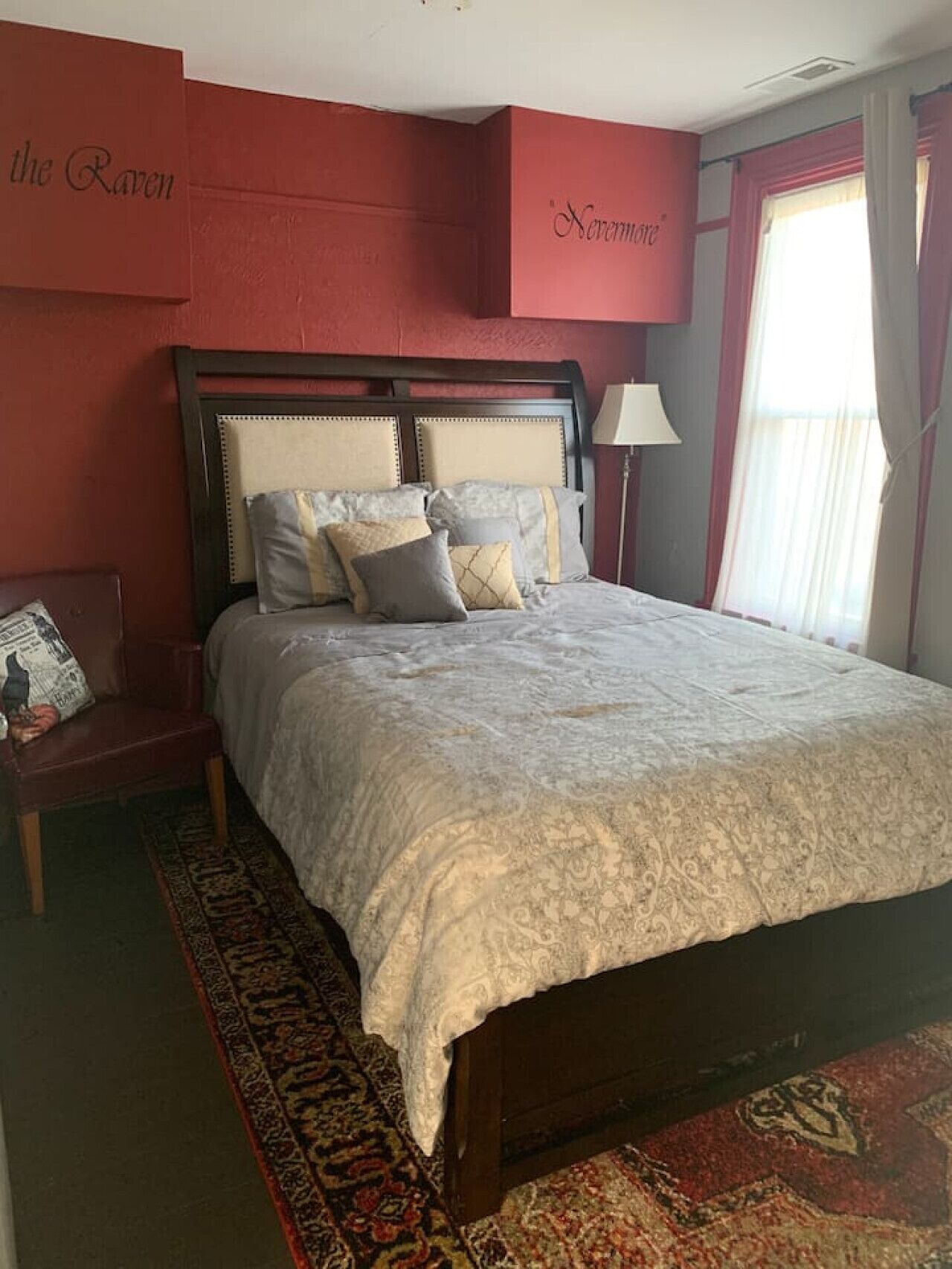 A bedroom with a large bed, a nightstand, a lamp, and a red accent wall.