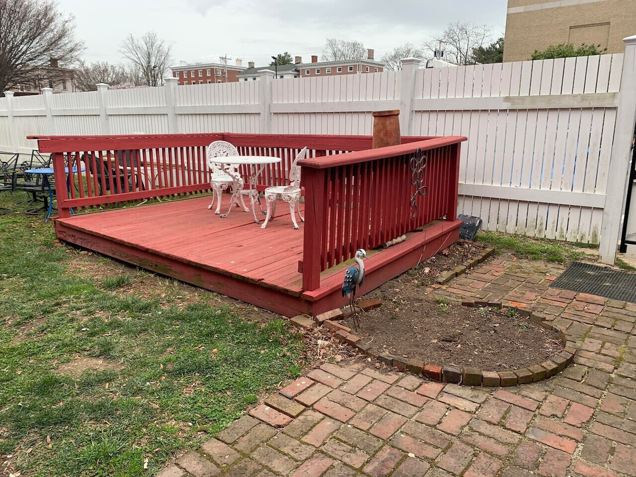 A red deck with white chairs and a small table, surrounded by a white fence.