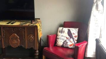 A living room with a red leather chair, a wooden cabinet, a television, and framed artwork on the wall.