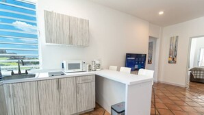 Una cucina moderna con un piano di lavoro bianco, un forno a microonde, una macchina da caffè e un lavello. È presente un'ampia finestra con vista sull'esterno.