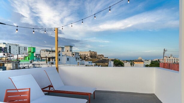 Una terrazza sul tetto con poltrone da relax bianche e un tavolo, con vista su un panorama urbano ricco di edifici storici e un cielo sereno.