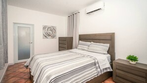 Una camera da letto con un letto, un comodino, una cassettiera, un condizionatore d'aria a parete e una porta con pannello in vetro satinato.