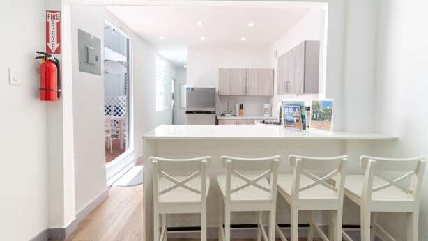 A modern kitchen with white cabinetry, a central island with chairs, and a fire extinguisher on the wall.
