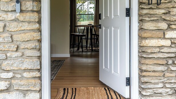 A stone exterior with a white door, a welcome mat, and two wall-mounted lanterns. - Charming Kentucky Stone House (Lexington)