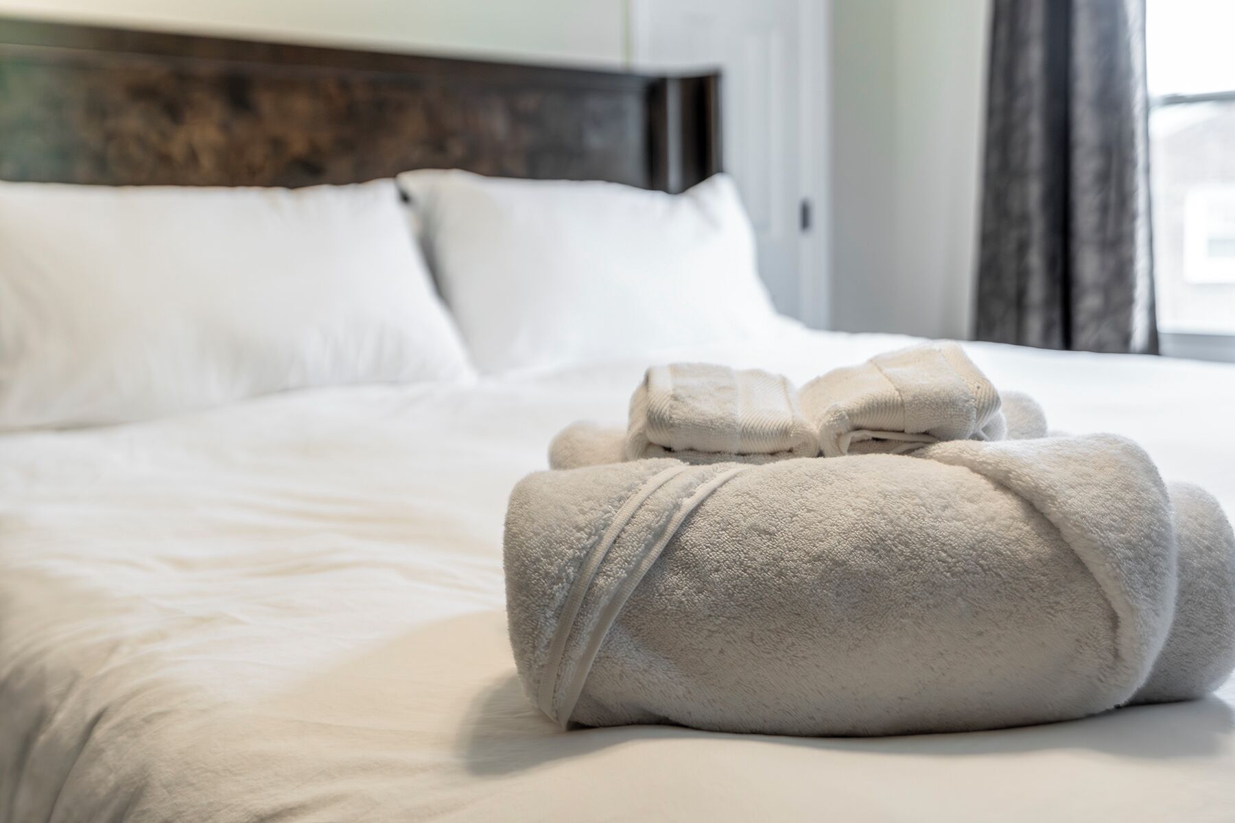 A neatly made bed with white linens and a set of towels on the bed.