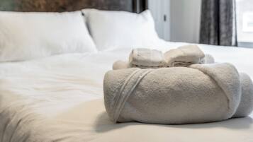 A neatly made bed with white linens and a set of towels on the bed.