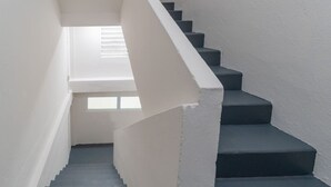 Eine Treppe mit weißen Wänden und dunklen Stufen, die zu einer Zwischenebene mit einem Fenster führt.