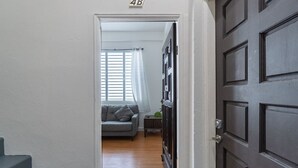 A hallway leading to a living room with a sofa, a small table, and a window with blinds. - Modern 2-BR Apt. in historic Old San Juan (San Juan)