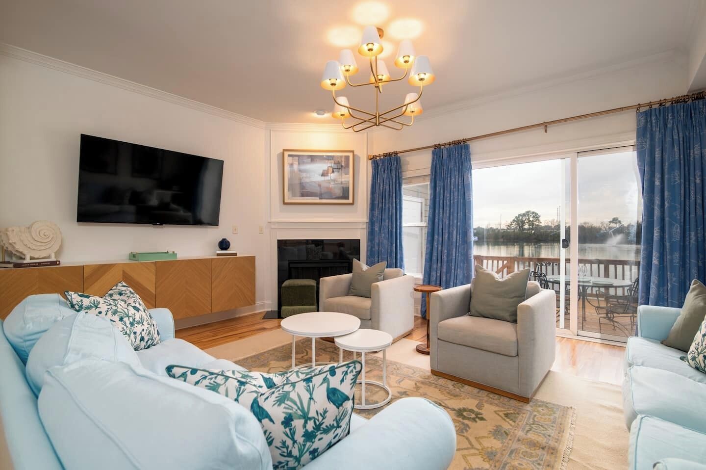 A spacious living room with a flat-screen TV, a fireplace, and a balcony with a view of a body of water.