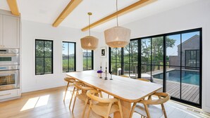 A modern kitchen with built-in appliances, a large dining table with wooden chairs, and a view of a swimming pool through large windows.