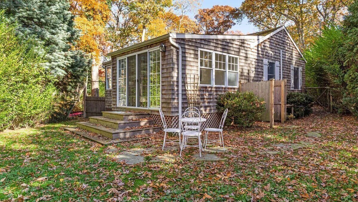 Een klein houten huis met een veranda en tuin.