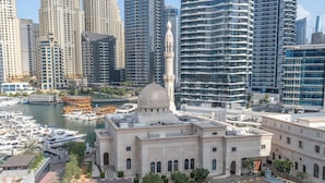 Um edifício histórico com cúpula e minarete, rodeado por edifícios modernos altos e uma marina com barcos.