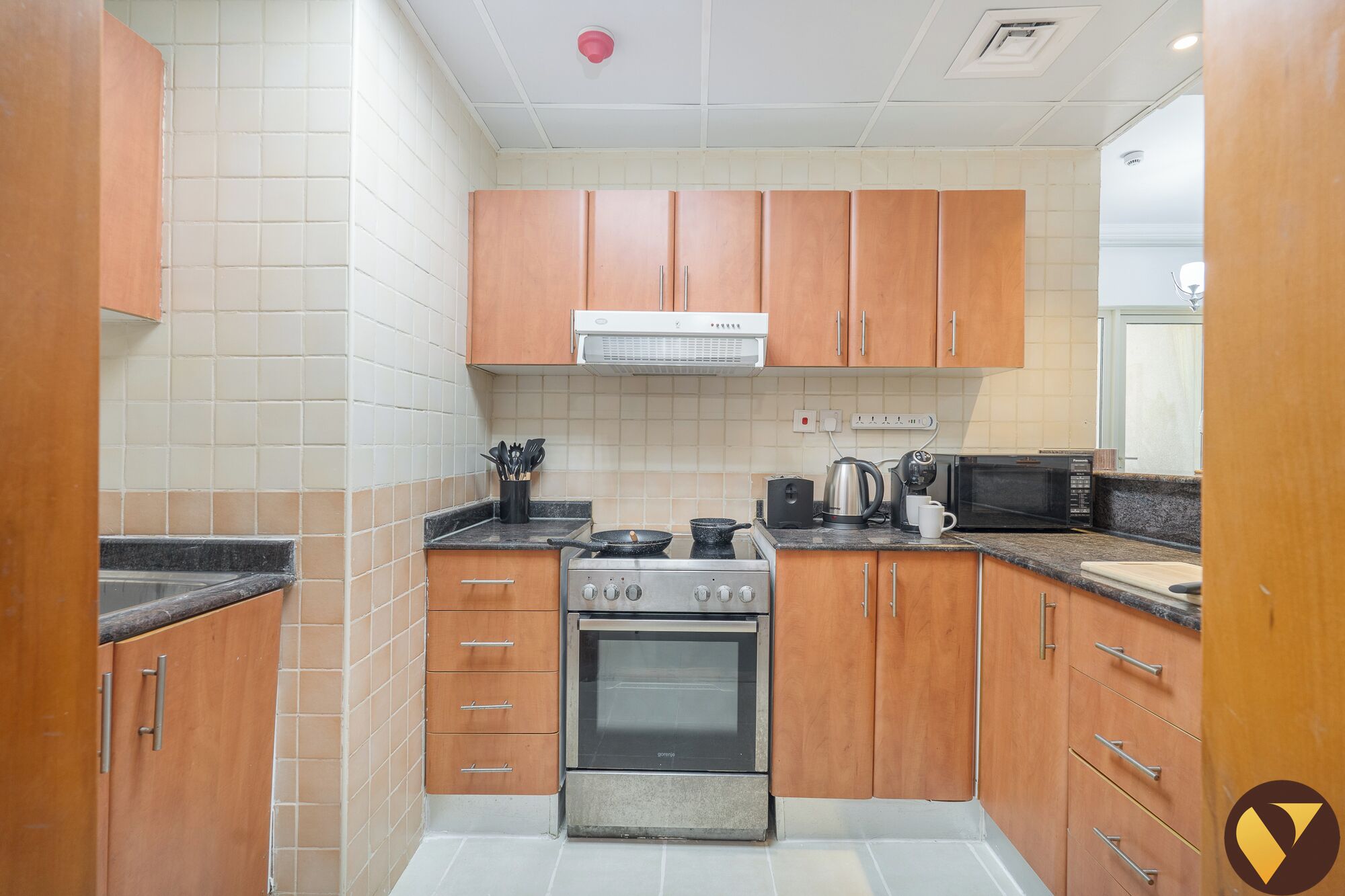 A compact kitchen with wooden cabinets, a gas stove, an oven, a microwave, and a coffee maker.