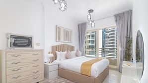 Quarto moderno com cama, cômoda, mesa de cabeceira e uma grande janela com vista para a cidade.