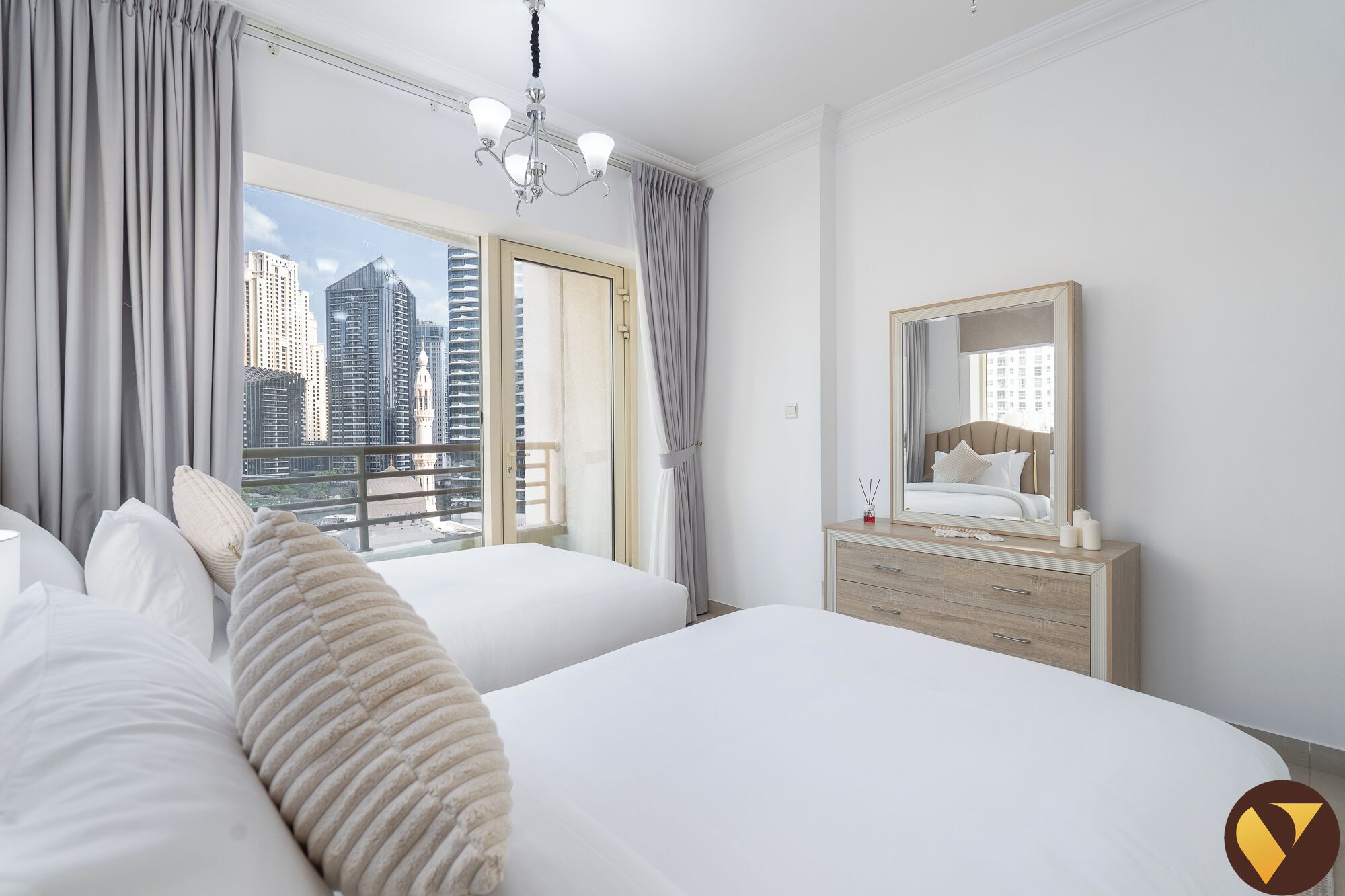 A hotel room with two beds, a dresser, a mirror, and a view of tall buildings.