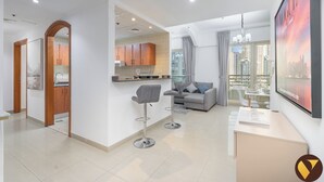 Um apartamento moderno com cozinha, sala de jantar e sala de estar. Possui uma janela grande com vista para a cidade, um sofá cinzento e uma mesa de jantar com cadeiras.