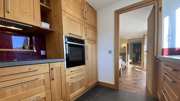 A kitchen with wooden cabinets, a black oven, and a tiled floor. - 2nd floor, balcony, tv, ski locker, 55m², Praz sur Arly (Praz-sur-Arly)