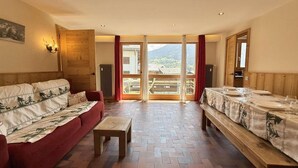 A spacious room with a wooden floor, a red sofa, a wooden bench, and a dining table set for two. - 2nd floor, balcony, tv, ski locker, 55m², Praz sur Arly (Praz-sur-Arly)