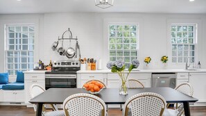 Uma cozinha moderna com armários brancos, fogão e uma área de refeições com mesa e cadeiras.
