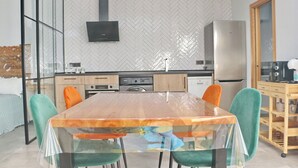 A modern kitchen with a large wooden table, teal chairs, and a herringbone-patterned backsplash.