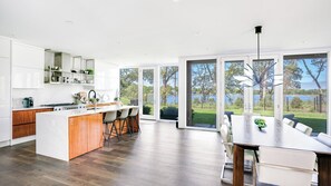 A modern kitchen with a central island, bar stools, and a dining area with a view of the outdoors.