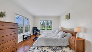 A bedroom with a bed, bedside tables, a dresser, a chair, and a window with a view of trees. - Cozy North Fork Home Among the Best Wineries in the Northeast, Minutes to... (Aquebogue)
