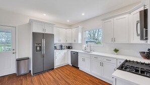 A modern kitchen with white cabinets, stainless steel appliances, and a wooden floor. - Cozy North Fork Home Among the Best Wineries in the Northeast, Minutes to... (Aquebogue)