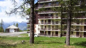 A multi-story hotel with balconies, surrounded by trees and a mountainous backdrop. - 50m from ski slopes, floor -1, terrace, tv, ski locker, 45m², Risoul (Risoul)