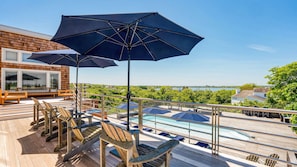 Une terrasse avec des chaises en bois et des parasols, une piscine et une vue sur le paysage.