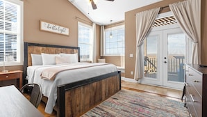 A bedroom with a wooden headboard, a bed with white bedding, a ceiling fan, and a view of a balcony through a glass door. - Penthouse Table Rock Lake View  Near SDC (Branson)