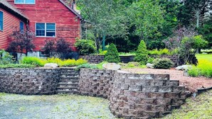 Una casa de madera roja con un muro de piedra de contención y un jardín con diversas plantas y arbustos.