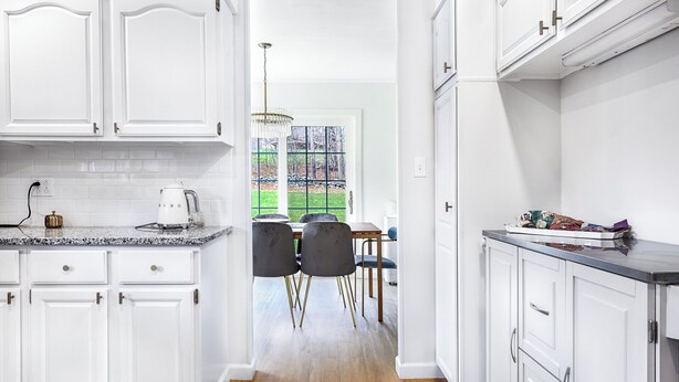 Una cocina moderna con armarios blancos, encimeras de granito y un comedor con vistas a un paisaje verde.