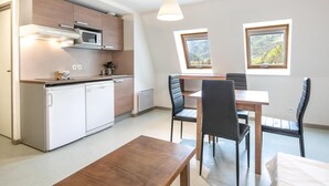 Ett kompakt kök med moderna vitvaror, en matplats med ett träbord och stolar samt ett fönster med utsikt över omgivningen.