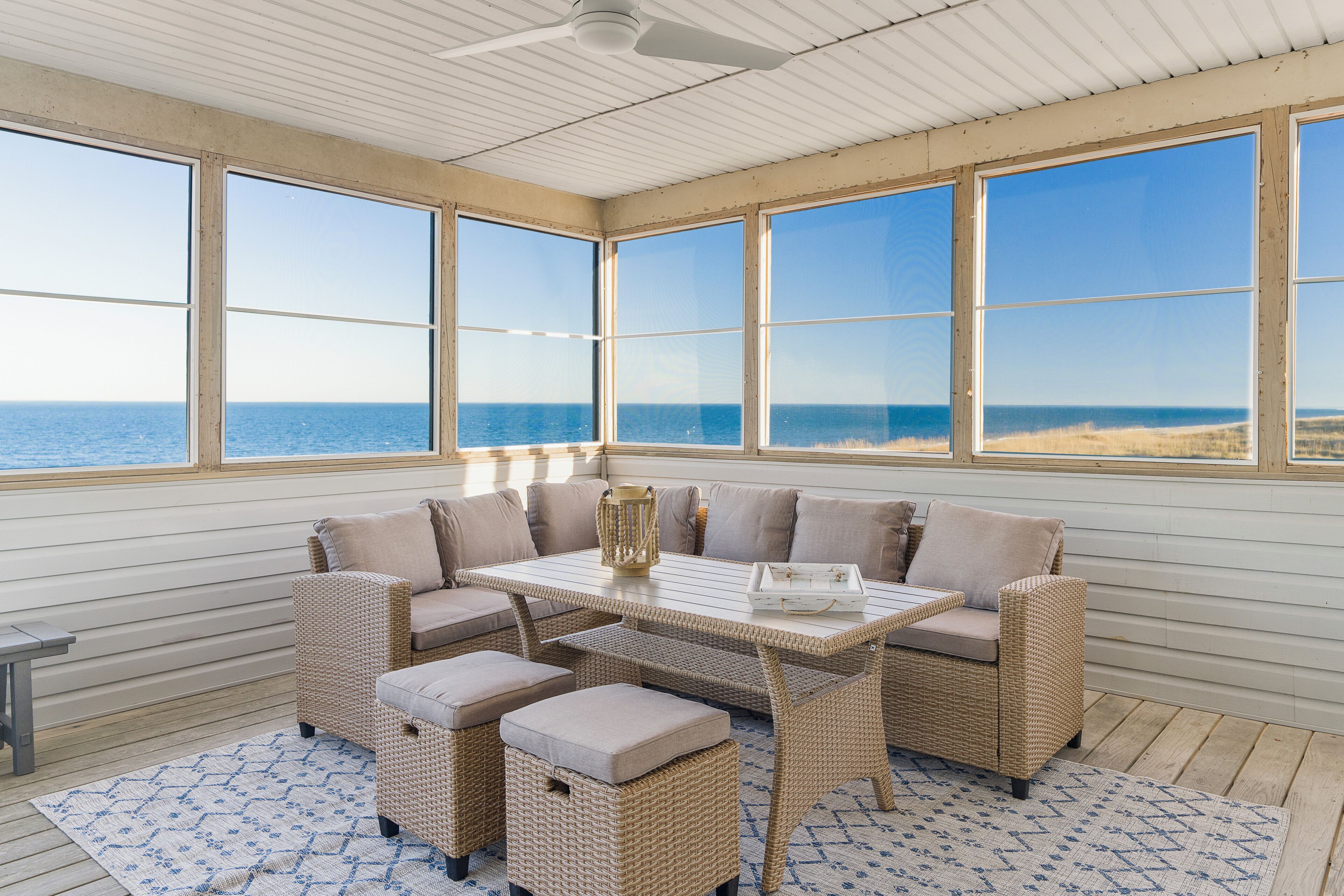A sunlit room with a large window overlooking the ocean, featuring a wicker sofa set and a small table.