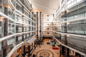 Um átrio com vários níveis, guarda-corpos de vidro, um espaço central aberto com assentos e um padrão circular no chão.