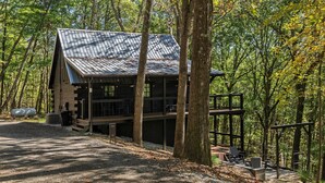 Une cabane avec un toit en métal, entourée d’arbres, et un chemin de gravier menant à celle-ci.