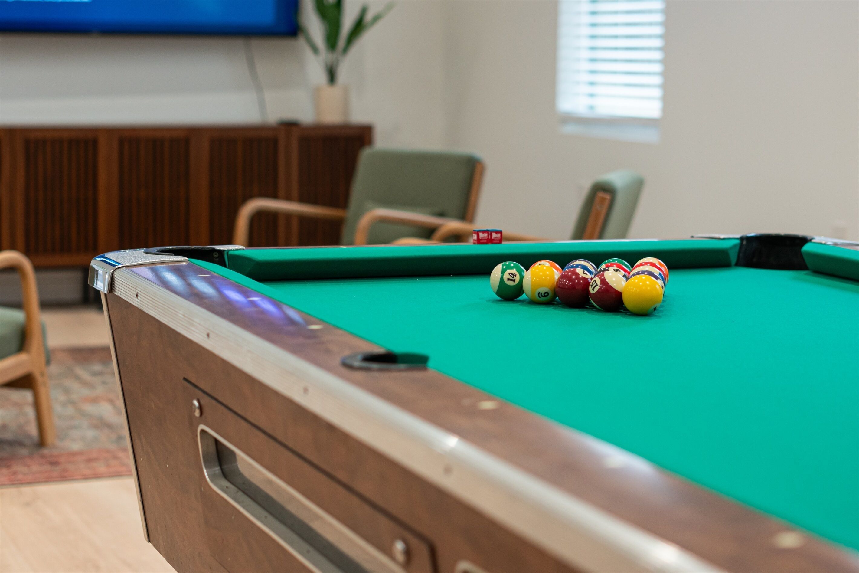 Una mesa de billar con bolas en una habitación con muebles de madera y un televisor al fondo.