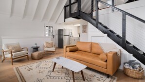 Un loft spacieux avec un plafond haut, un escalier noir, un canapé beige, une table basse blanche et un coin cuisine.