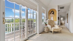A spacious room with large windows, a balcony, a classic armchair, and a painting on the wall.