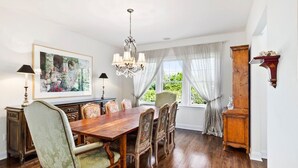 A dining room with a wooden table, chairs, a chandelier, and a large window with curtains.