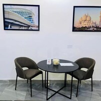 Quarto com duas imagens emolduradas de edifícios, uma mesa redonda com cadeiras e uma tigela de vidro sobre a mesa.
