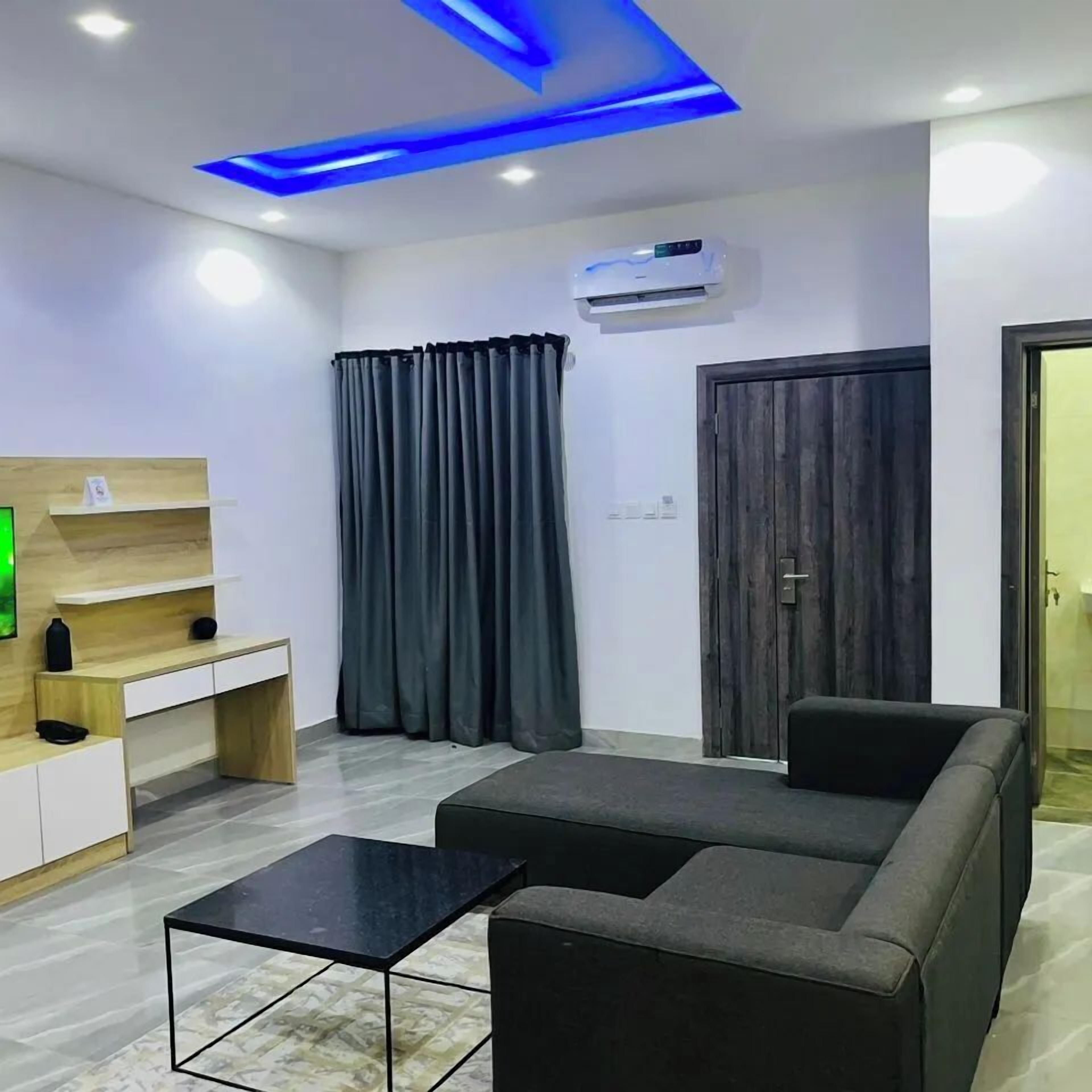 Una sala de estar moderna con un sofá, una mesa de centro, un televisor sobre una estantería de madera y una puerta con paneles de madera oscura.