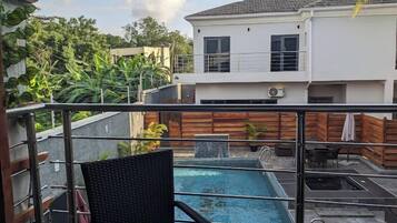 A rooftop pool area with a chair and table, surrounded by a wooden fence and a white building in the background.