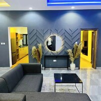 Um lobby moderno com sofá, mesa de centro e uma parede decorativa com espelho e capim-dos-pampas.