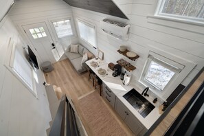 A compact kitchen with white cabinetry, a dining area with a table and chairs, and a large window providing natural light.