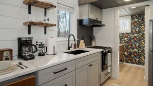 Eine moderne Küche mit weißen Schränken, einer großen Kochinsel inklusive Spüle und einer Kaffeemaschine. Darüber befinden sich Holzregale und eine dekorative Spritzschutzwand.